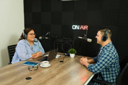 Foto de Mujer feliz transmitida con un programa de radio teniendo una entrevista con un hombre latino y un invitado de podcast - Imagen libre de derechos