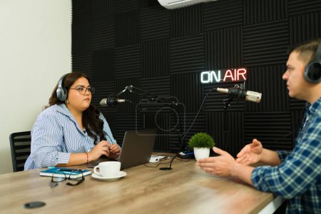 Téléchargez les photos : Femme séduisante écoutant son invité podcast lors d'une interview pour son talk-show dans le studio d'enregistrement - en image libre de droit