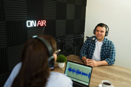 Photo for Handsome latin guest in the radio soundproof studio talking to the podcast host and enjoying the talk show recording - Royalty Free Image