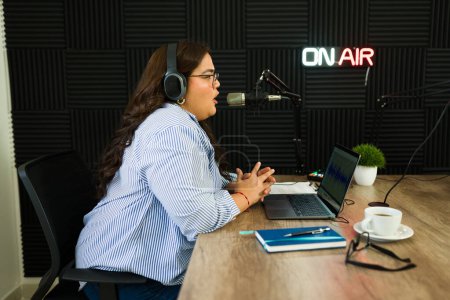 Photo for Latin woman and radio host in the recording studio talking with a podcast guest during her talk show - Royalty Free Image
