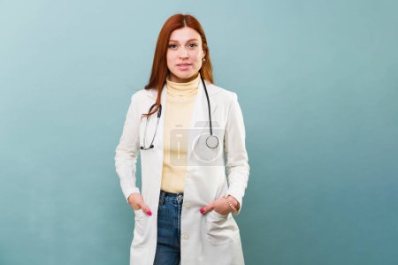 Téléchargez les photos : Roux rousse roux femme médecin dans la trentaine avec un blouse de laboratoire portant un blouse de laboratoire et stéthoscope souriant et l'air heureux - en image libre de droit
