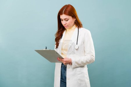 Photo for Professional redhead doctor with a lab coat writing on the medical record after treating a sick patient - Royalty Free Image