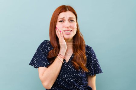 Téléchargez les photos : Inquiète roux femme dans la trentaine souffrant de douleur dentaire et voulant aller chez le dentiste toucher le côté de son visage - en image libre de droit