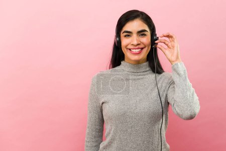 Foto de Hermosa mujer hispana sonriendo usando un auricular mientras trabajaba en el centro de llamadas como agente de servicio al cliente - Imagen libre de derechos