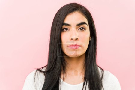 Foto de Primer plano de una atractiva mujer latina de unos 30 años con una expresión seria mirando a la cámara sobre un fondo rosa - Imagen libre de derechos