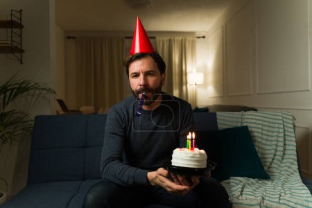 Foto de Triste hombre caucásico con un sombrero de fiesta teniendo una celebración de cumpleaños solo mientras se siente solo en casa - Imagen libre de derechos