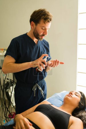 Foto de Atractivo terapeuta poniendo crema hidratante a una mujer después de un tratamiento de belleza o terapia alternativa en la clínica de salud - Imagen libre de derechos