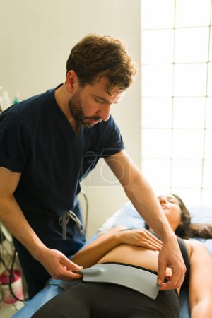 Hispanic therapist with a female patient preparing electromedical therapy and radiofrequency at the alternative health clinic