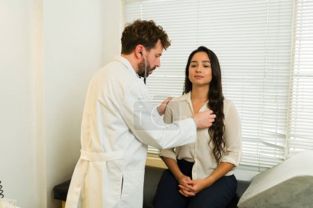 Foto de Médico que usa el estetoscopio y revisa el corazón de un hermoso paciente latino durante una consulta de chequeo médico en la clínica - Imagen libre de derechos