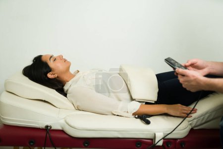 Hispanic woman getting a massage andullation therapy using vibration machine at the alternative medicine clinic