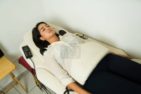 Foto de Vista superior de una mujer hispana relajada recibiendo un masaje biofísico de vibración durante la terapia de andulación en la clínica de bienestar - Imagen libre de derechos