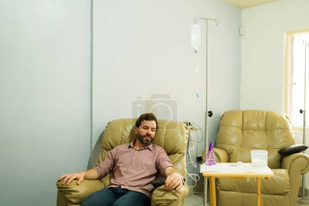 Happy hispanic man smiling at the health wellness clinic getting IV drip therapy and myers vitamins cocktail for a healing treatment
