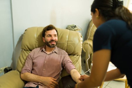 Attraktiver glücklicher Mann im Gespräch mit der Krankenschwester, während er alternative Medizin und IV-Tropftherapie für einen myers Vitamincocktail bekommt