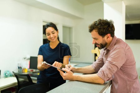 Hombre sonriente mirando emocionados firmando papeles con una enfermera antes de un tratamiento alternativo de bienestar en la clínica de salud 