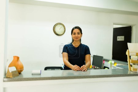 Photo for Attractive happy nurse receptionist working at the health clinic looking cheerful and smiling waiting for a patient and start a medical treatment - Royalty Free Image