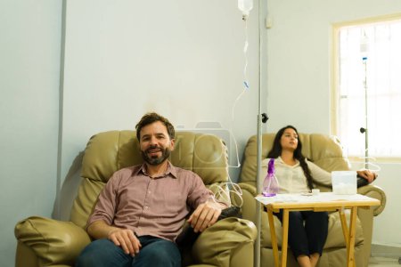 Handsome latin man and woman at the health clinic getting an IV drip with myers cocktail looking happy about their health and wellness
