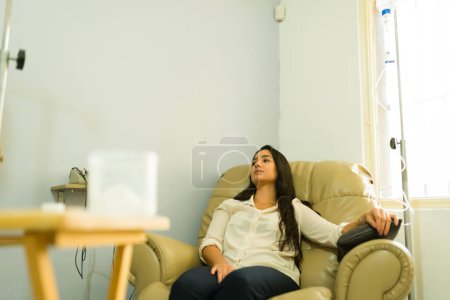 Photo for Sick latin woman getting IV drip and vitaminized serum with myers cocktail for a system detox at the wellness clinic - Royalty Free Image
