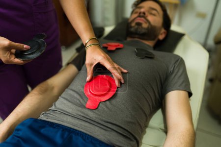 Foto de Hombre hispano recibiendo terapia de medicina alternativa y probando terapia de campo magnético con su terapeuta o médico para aliviar el dolor - Imagen libre de derechos
