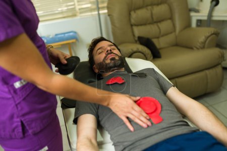 Relaxed man with a therapist getting magnet therapy on his abdomen to relieve pain and trying alternative medicine 