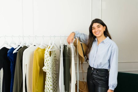 Photo for Cheerful Latin young woman browsing through clothes in a fashionable boutique - Royalty Free Image