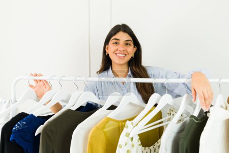 Téléchargez les photos : Joyeux jeune femme choisir des vêtements à partir d'un rack, profiter du shopping - en image libre de droit