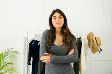 Téléchargez les photos : Jeune femme en tenue décontractée se tient fièrement dans son espace de travail bien organisé de conception de mode - en image libre de droit