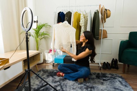 Photo for Young woman showcases apparel while filming for her fashion vlog at home - Royalty Free Image