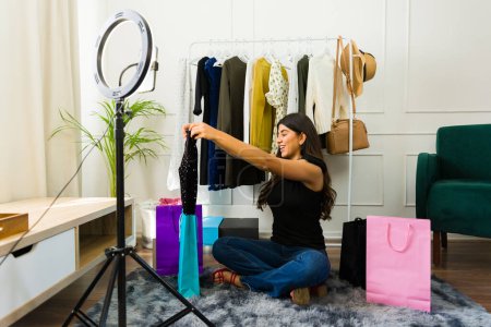 Young woman recording a fashion haul video for her blog, surrounded by shopping bags