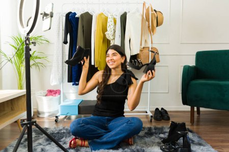 Téléchargez les photos : Gai influenceur féminin examinant les chaussures à la mode dans son confortable studio à la maison - en image libre de droit