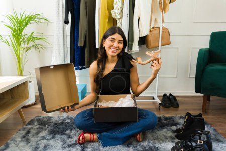 Photo for Smiling young Hispanic woman sitting on floor, showcasing her new pair of shoes with box - Royalty Free Image