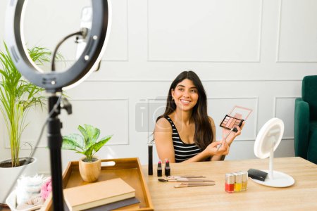 Foto de Mujer sonriente muestra cosméticos durante un tutorial en línea con luz de anillo y cámara - Imagen libre de derechos