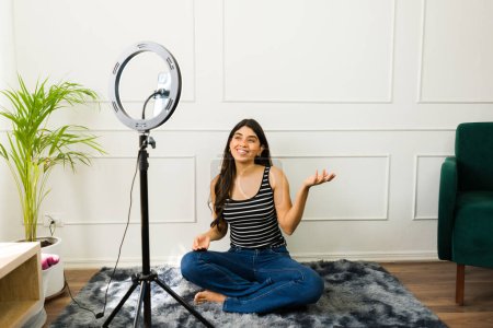 Photo for Smiling female content creator recording a video blog in a cozy living room setup - Royalty Free Image