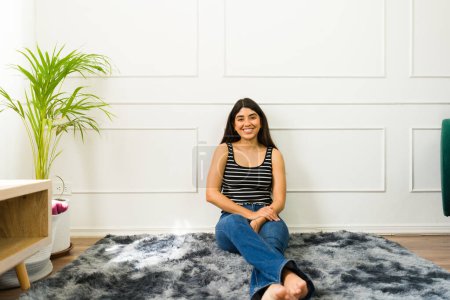 Photo for Cheerful young woman sitting on a rug with a cozy home interior background - Royalty Free Image