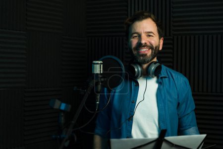 Photo for Cheerful man with headphones recording audio in a professional sound booth - Royalty Free Image