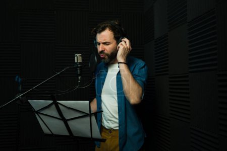 Focused male voice actor with headphones recording audio in a professional studio