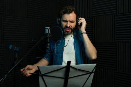 Man with headphones singing passionately into a studio microphone, surrounded by acoustic foam