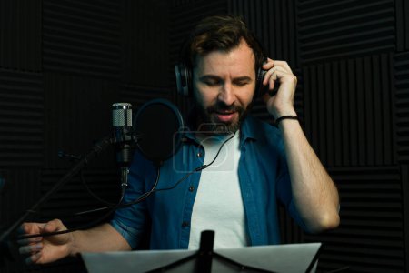 Focused man records audio while reading a script in a professional soundproof studio