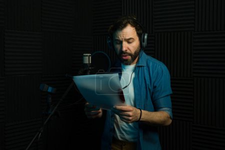 Acteur vocal masculin concentré effectue la lecture de script dans un microphone dans un studio professionnel
