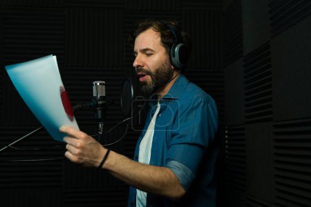 Male voiceover artist reading a script into a microphone inside a recording booth
