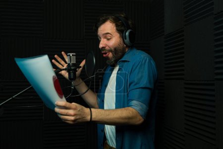 Male voice actor recording audio while holding a script in a professional studio equipped with soundproofing