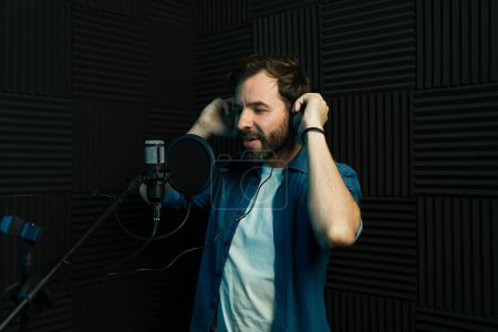 Männlicher Sänger mit Kopfhörer, der einen Song in einem professionellen Studio-Setting aufnimmt