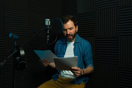Focused male voice actor reads from a script and gets ready to record in a professional studio setup