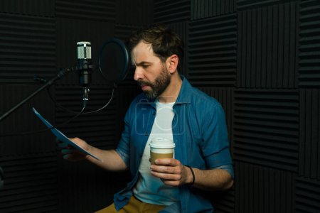 Focused man holding a script and coffee cup while getting ready to record in a professional studio