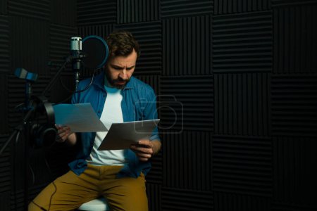 Hombre enfocado graba audio, guion de lectura en un estudio de grabación insonorizado