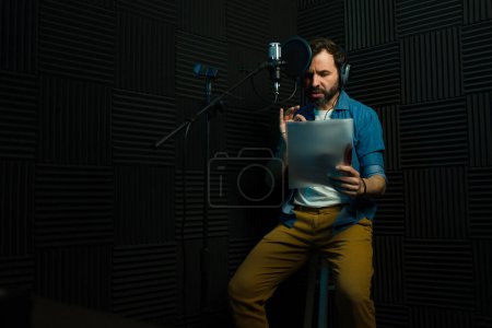 Engaged male voice actor records audio while reading a script in a soundproof studio