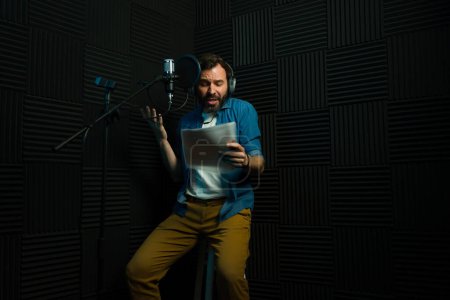Professional male voice artist performing script reading in a recording booth with microphone and acoustic foam