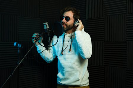 Téléchargez les photos : Chanteur masculin avec écouteurs dans un studio d'enregistrement insonorisé - en image libre de droit