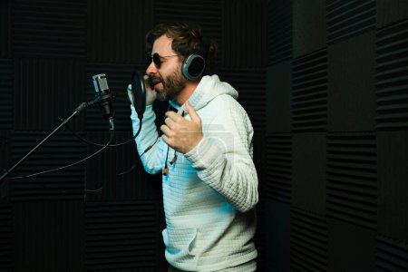 Téléchargez les photos : Joyeux chanteur masculin portant un casque se produit au microphone dans un studio d'enregistrement insonorisé - en image libre de droit