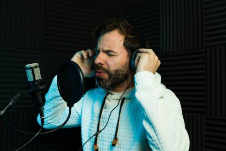Photo for Adult male singer performing into a microphone in a studio with headphones on - Royalty Free Image
