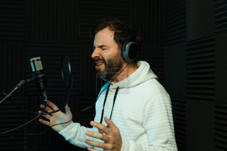 Enthusiastic male singer with headphones performs in a soundproof recording studio